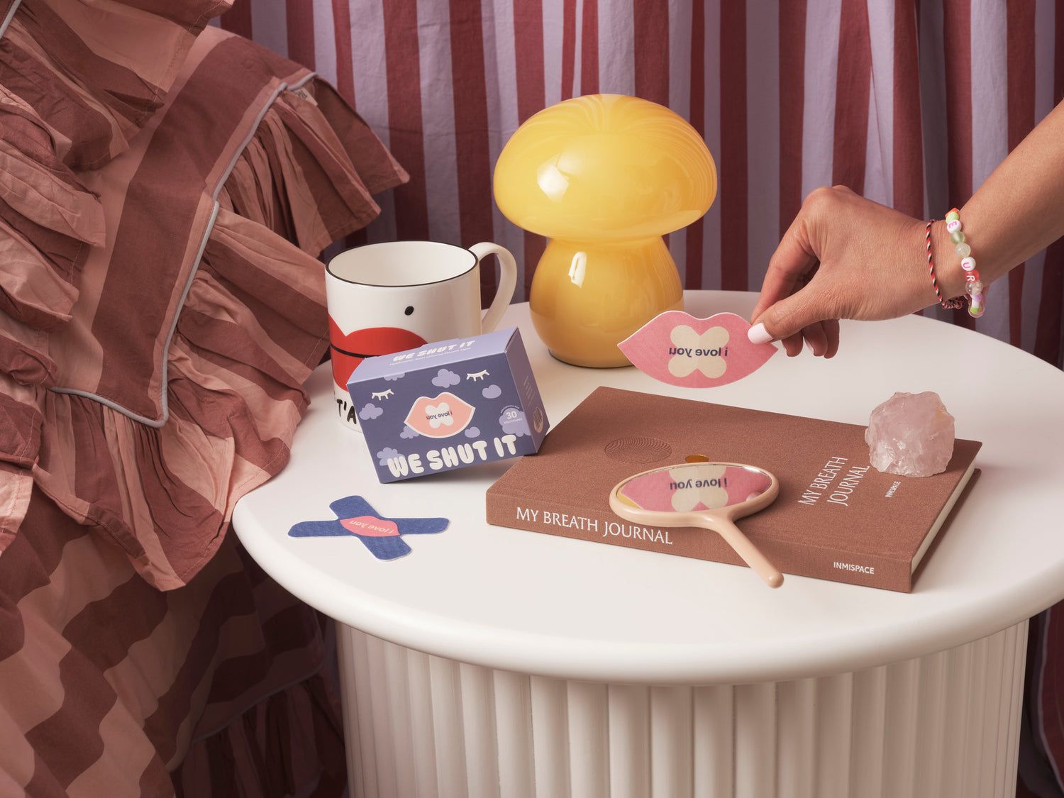 A table with we shut it mouth tapes, a mug, a lamp, and books with visible text in a casual setting.