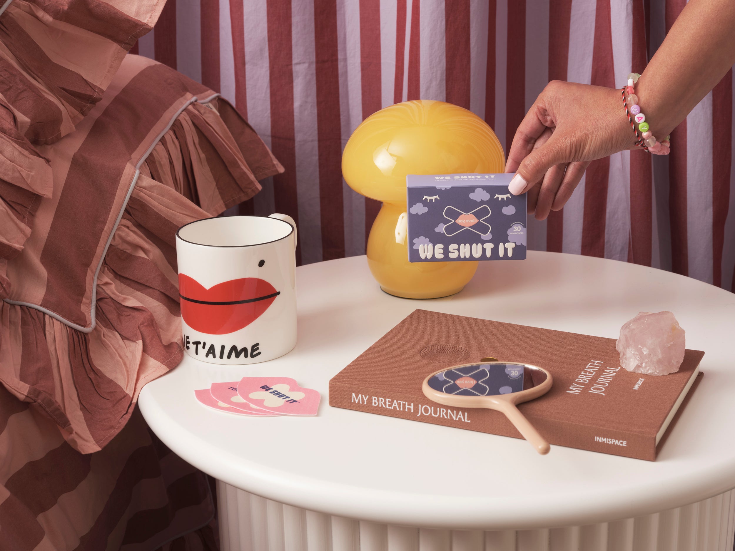 A table with we shut it mouth tapes, a mug, a lamp, and books with visible text in a casual setting.