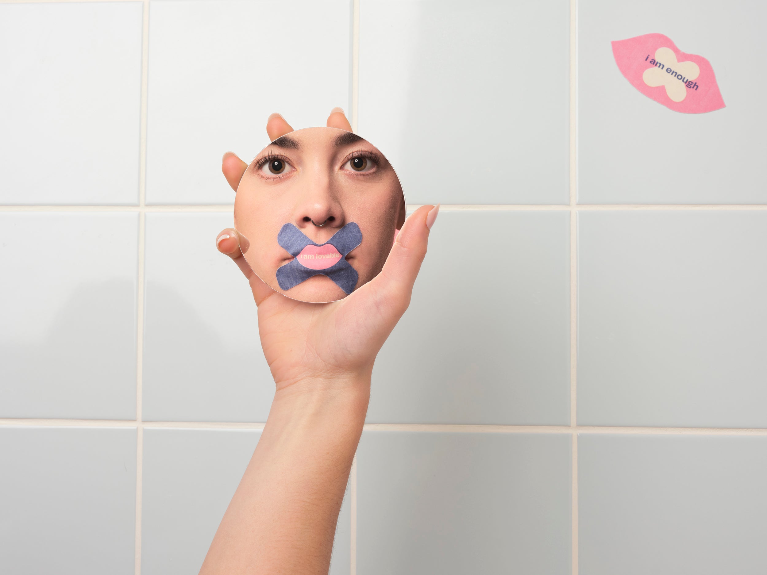 Person holding a hand with a lip mouth tape on a tiled bathroom wall.
