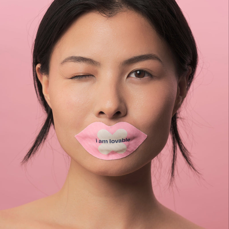 Woman with blue We Shut It mouth tape against a pink background