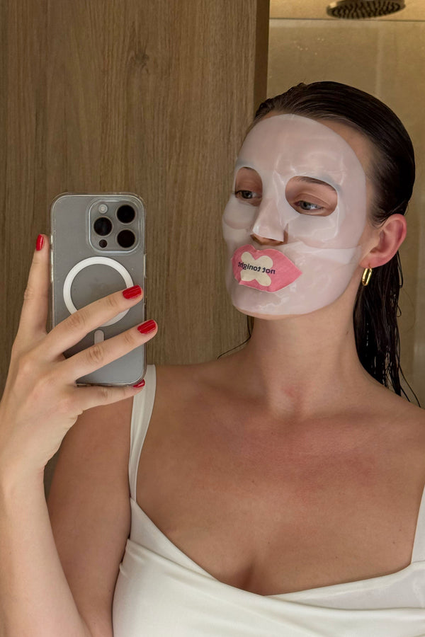A woman wearing We Shut It mouth tape and a face mask, taking a mirror selfie.
