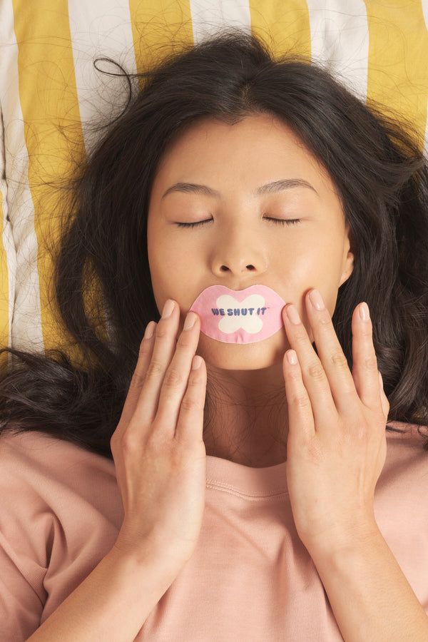 We Shut It bamboo mouth tape on a female model lying in bed with a striped duvet cover.