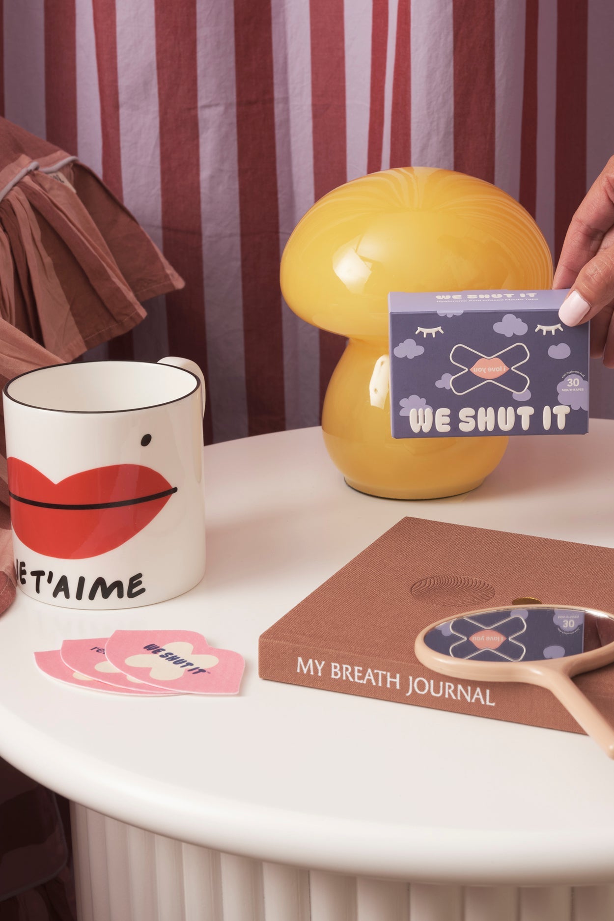 We Shut It bamboo fibre mouth tapes on a nightstand with a tea cup, a journal and a mirror.